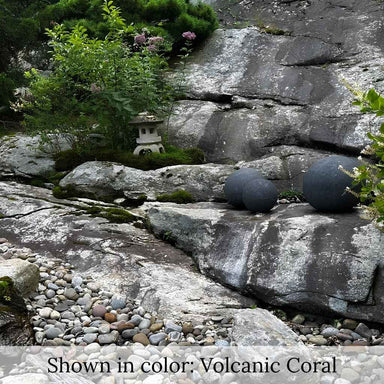 Three Angkor Garden Spheres resting on a natural rock ledge surrounded by lush greenery and a stone garden landscape.