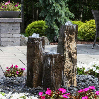 Bowled Top Basalt Fountain Kit on black pebbles beside pink flowers