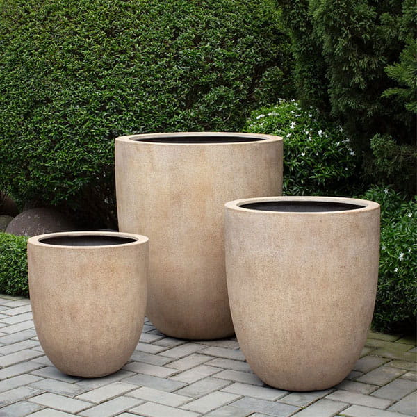 Bradford Planter in terra antique lite on concrete against green leaves.