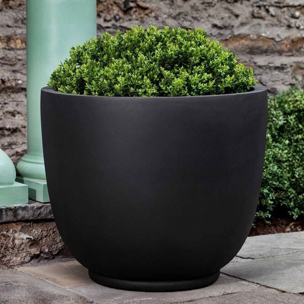 Danilo Planter, Extra Large in onyx black lite on concrete filled with plants.