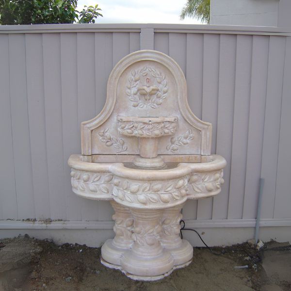 Deruta Lemon Wall Fountain in the backyard against white fence.