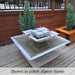 Facet Fountain with bubbling water cascading into a square basin on a wood deck surrounded by lush green plants in sideview.