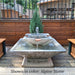 Facet Fountain with bubbling water cascading into a square basin on a wood deck surrounded by lush green plants upclose.
