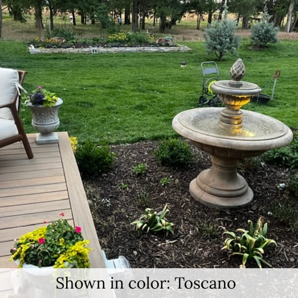 Fontana Grande outdoor fountain beside a backyard patio deck with garden landscaping at dusk.