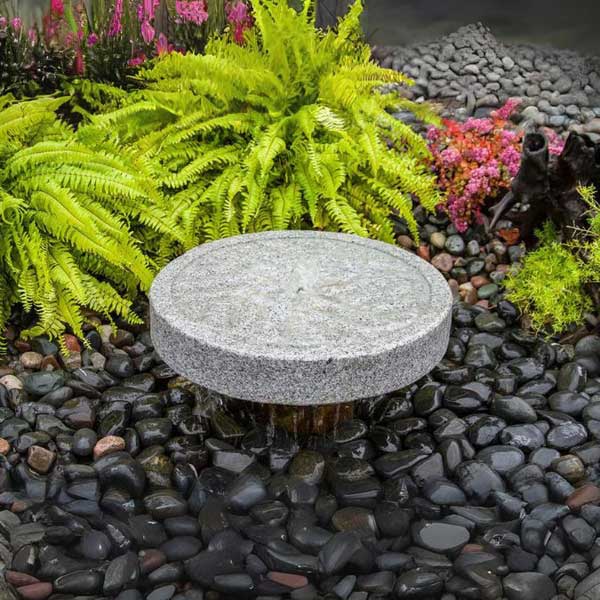 Millstone Fountain Kit Angled Style on black pebbles in the backyard