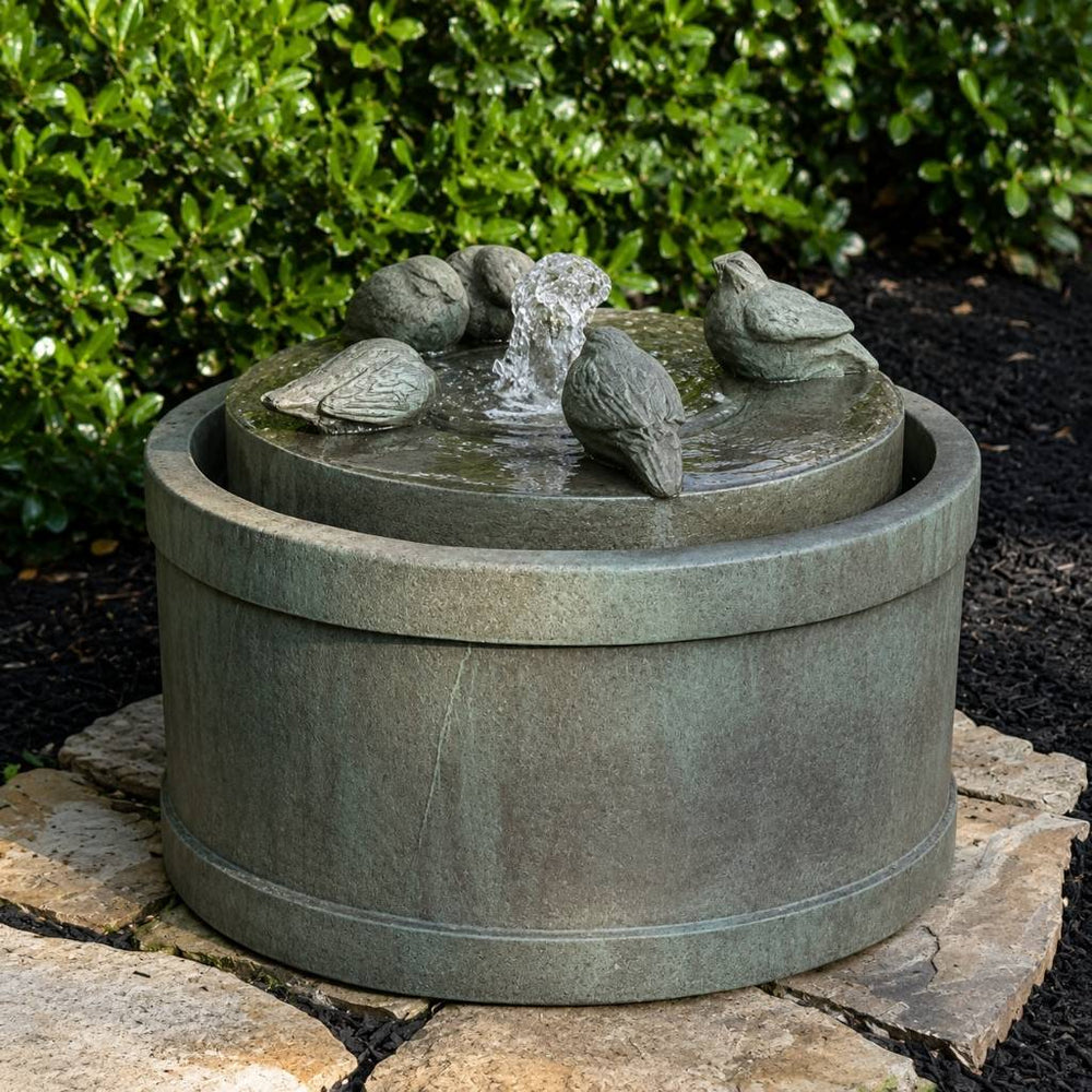 Passaros Fountain with 5 decorative birds perched around a bubbling water spout against a lush green shrub backdrop
