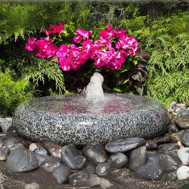 Smooth Round Fountain on black peebles against pink flowers