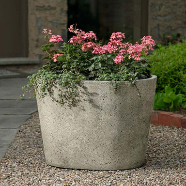 Tapered Oval Planter on gravel filled with pink flowers.