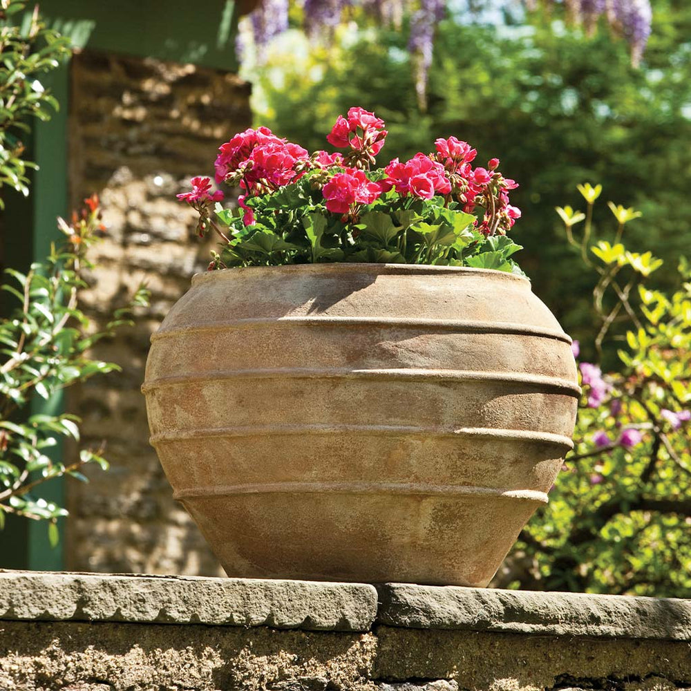 Thea Planter Antico Terra Cotta S/1 filled with pink flowersin the backyard