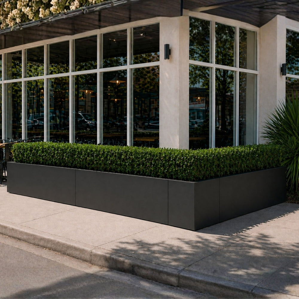 Tolga Modular Fiberglass Planters in matte charcoal with trimmed boxwood hedges lining a modern restaurant building exterior