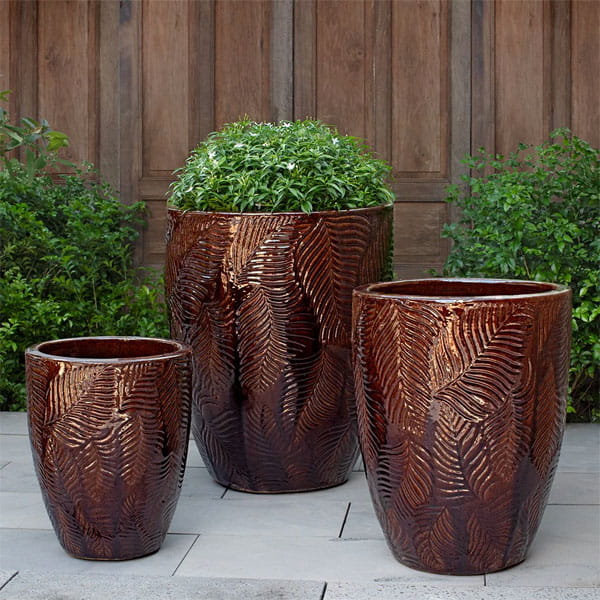 Tropicale Planter, Tall = Cognac on concrete filled with plants.