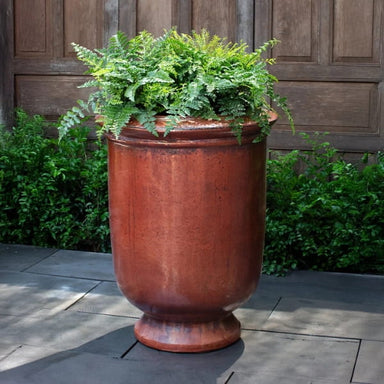 Vaucluse Urn in brunello color on concrete filled with plants.