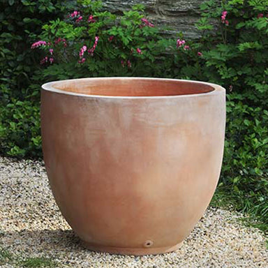 Causago Round Planter  - TC Set of 4 on gravel against concrete wall with plants