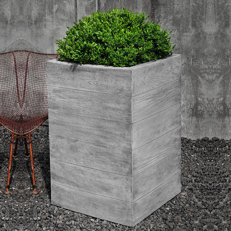 Chenes Brut Tall Box Planter filled with plants beside a chair