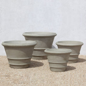 Classic Rolled Rim 31.5 inch Planter with three different sized planters on gravel against cream wall