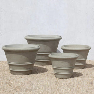 Classic Rolled Rim 35.5" Planter with three different sized planters on gravel against cream wall