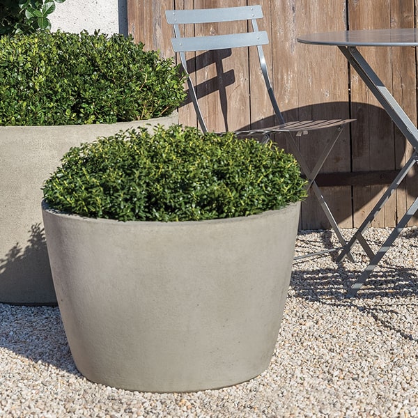 two big round planters filled with green plants next to table