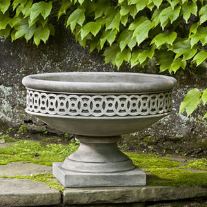 Williamsburg Low Fretwork Urn on concrete against wall with plants